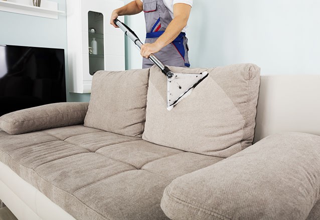Profissional higienizando um sofá bege com equipamento de extração