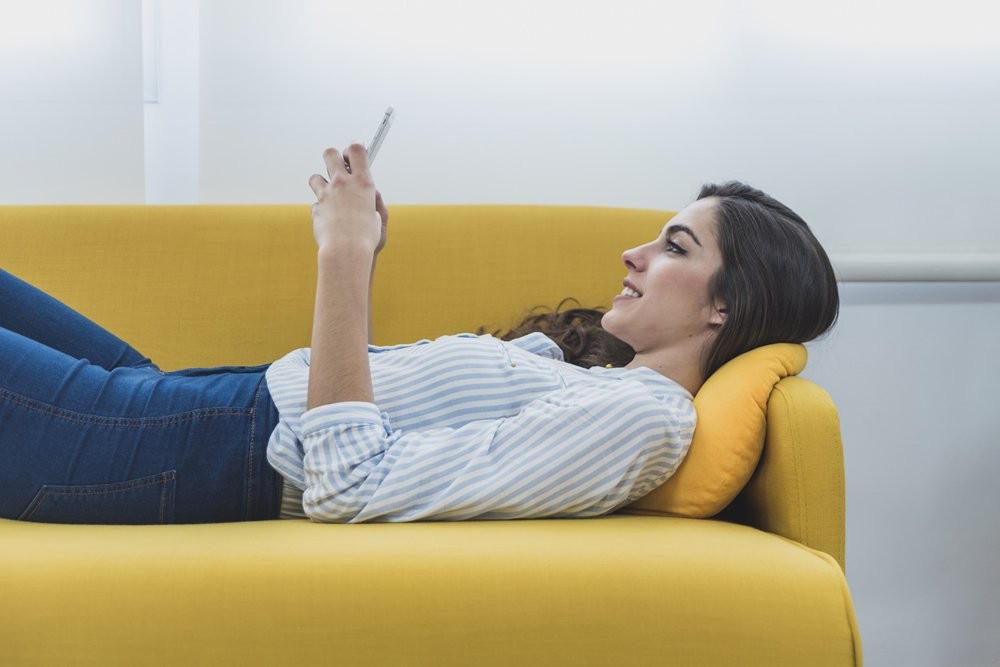Mulher deitada em um sofá amarelo usando o celular